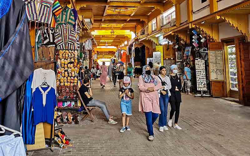 Un marché couvert animé dans la médina de Rabat, avec des étals de vêtements et des visiteurs.